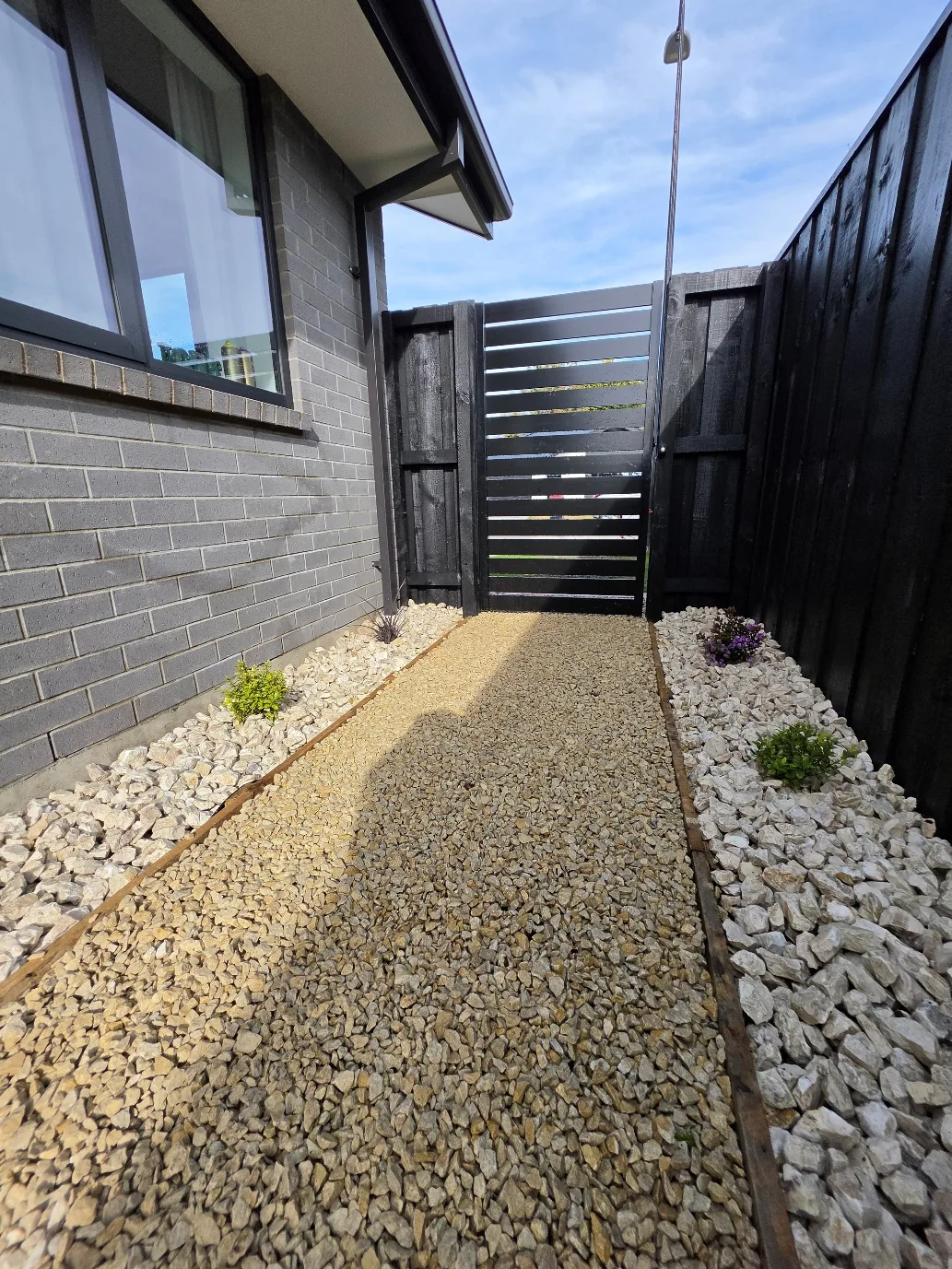 Side access path with decorative gravel, stone borders and black timber gate at 25 Derbridge Street