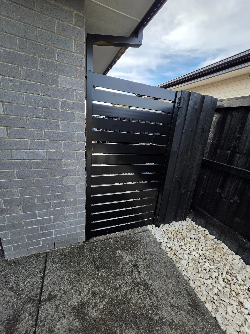 Black timber side gate with decorative stone and gravel at 25 Derbridge Street landscaping project