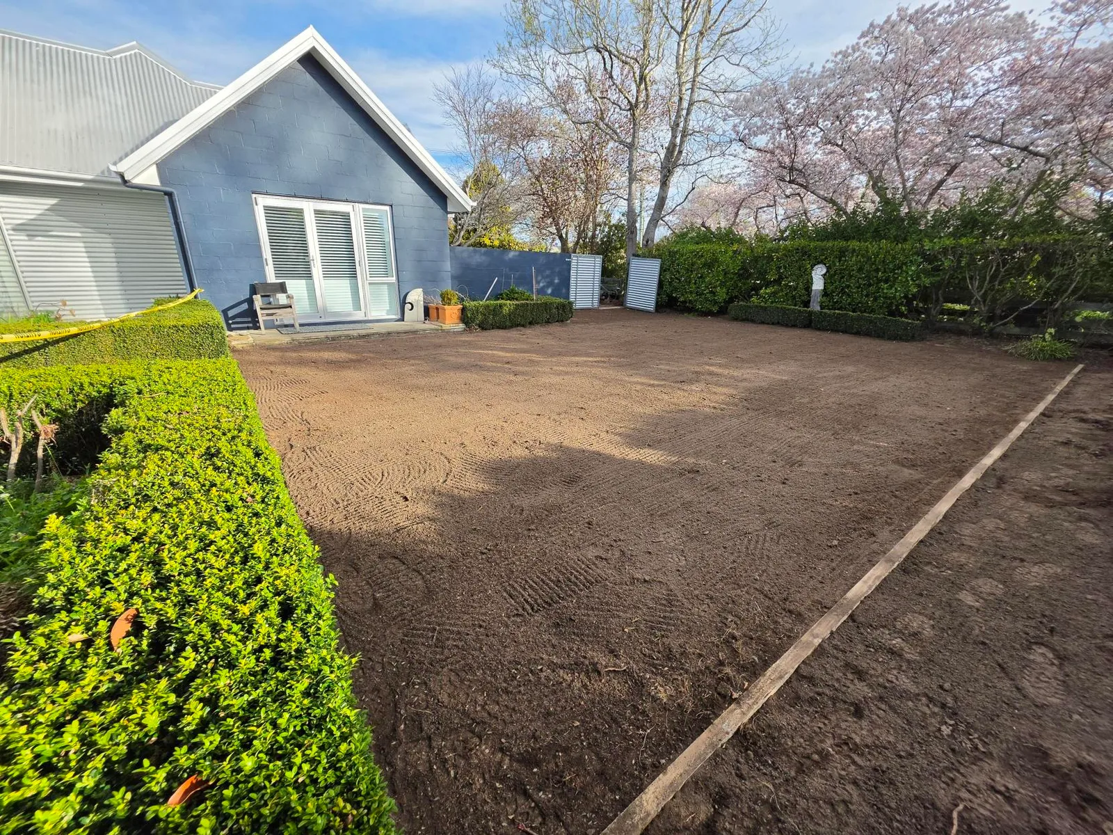 Completed lawn preparation showing levelled soil and straight timber edging along the side border, Canterbury