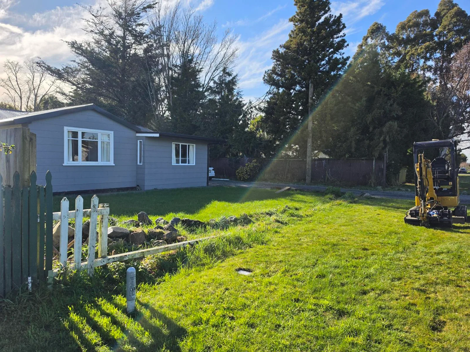 Mini excavator on the lawn before boundary fence replacement at Waddington, Canterbury
